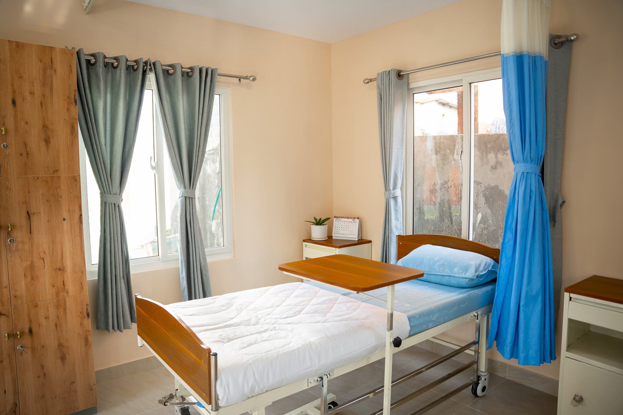 A private cabin at Naman Bansbari — a single hospital bed with wooden headboard and soft window light