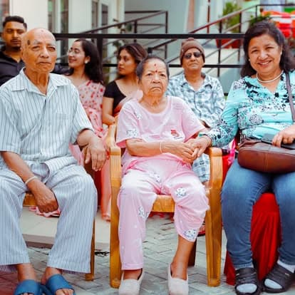 Elderly residents and visiting family seated together outdoors on the anniversary day