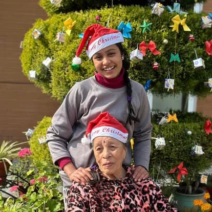 A Naman nurse and an elderly resident in matching Santa hats beside the Christmas tree