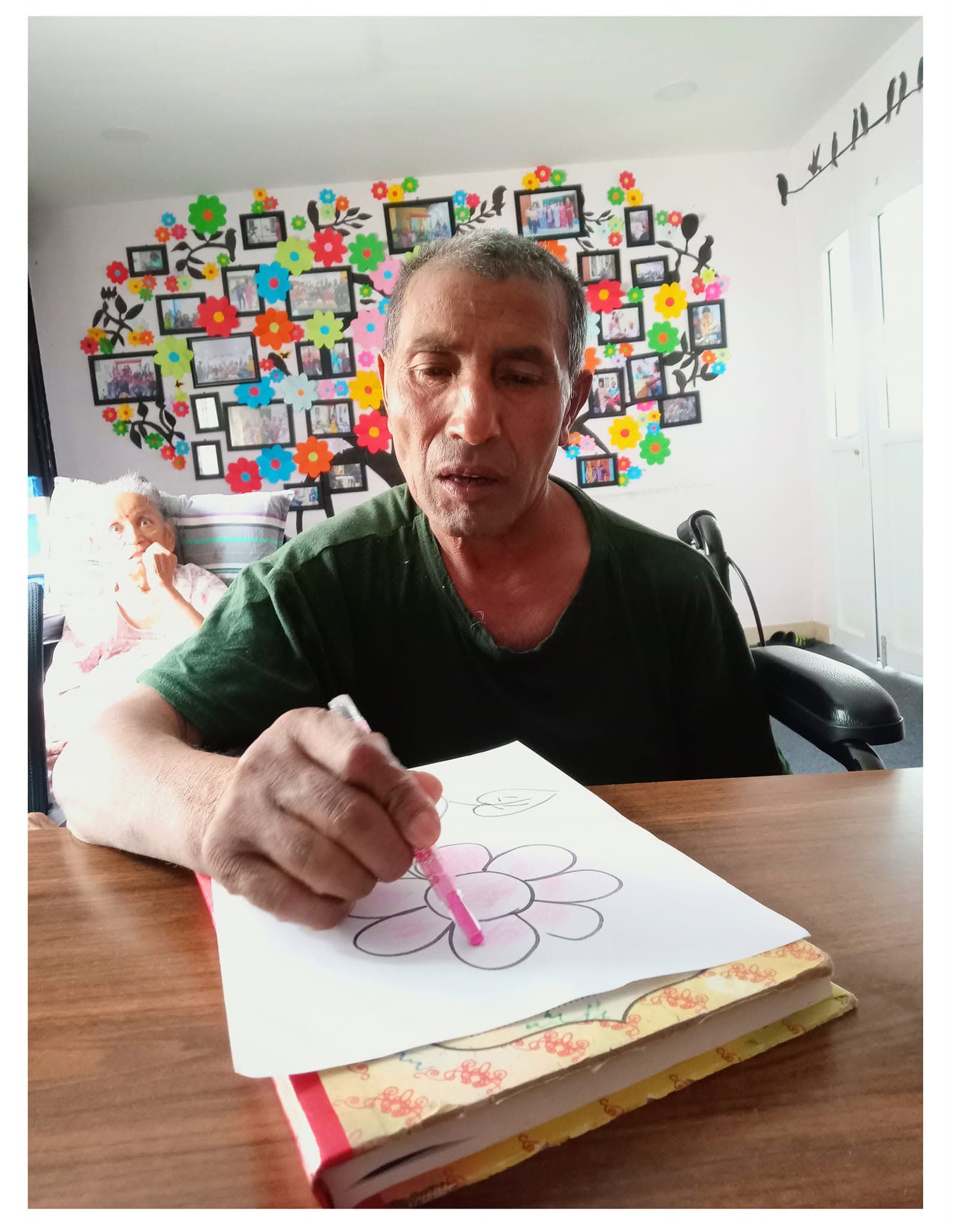 A Naman resident colouring a paper flower at the memory wall — a dementia-friendly activity