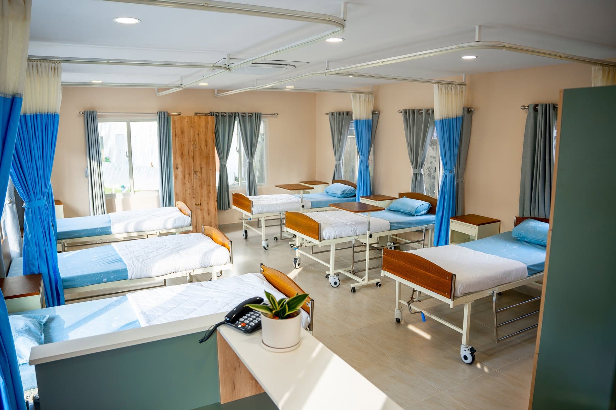 A sunlit ward with wooden hospital beds at Naman Care Home — steady, long-term care