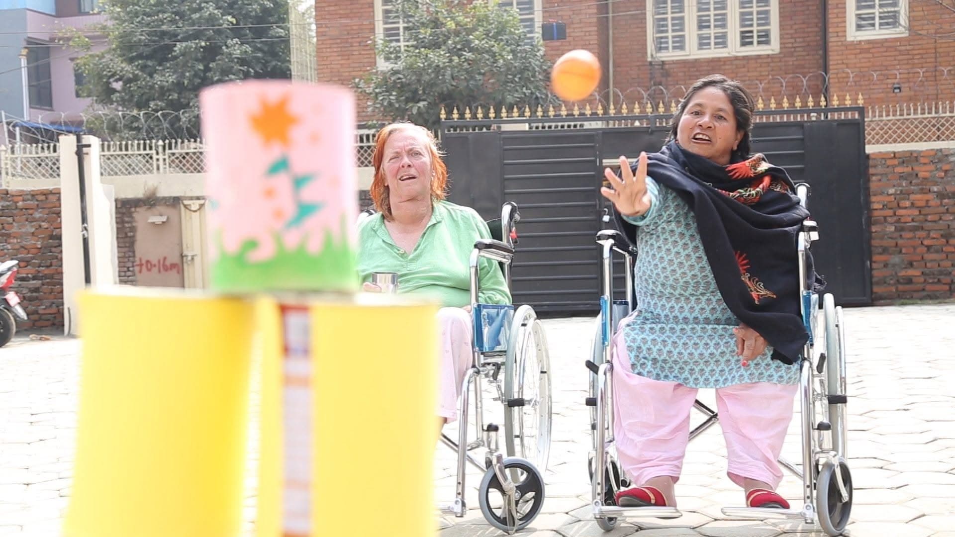 Two Naman residents playing a wheelchair ring-throw game outdoors — trauma recovery in motion