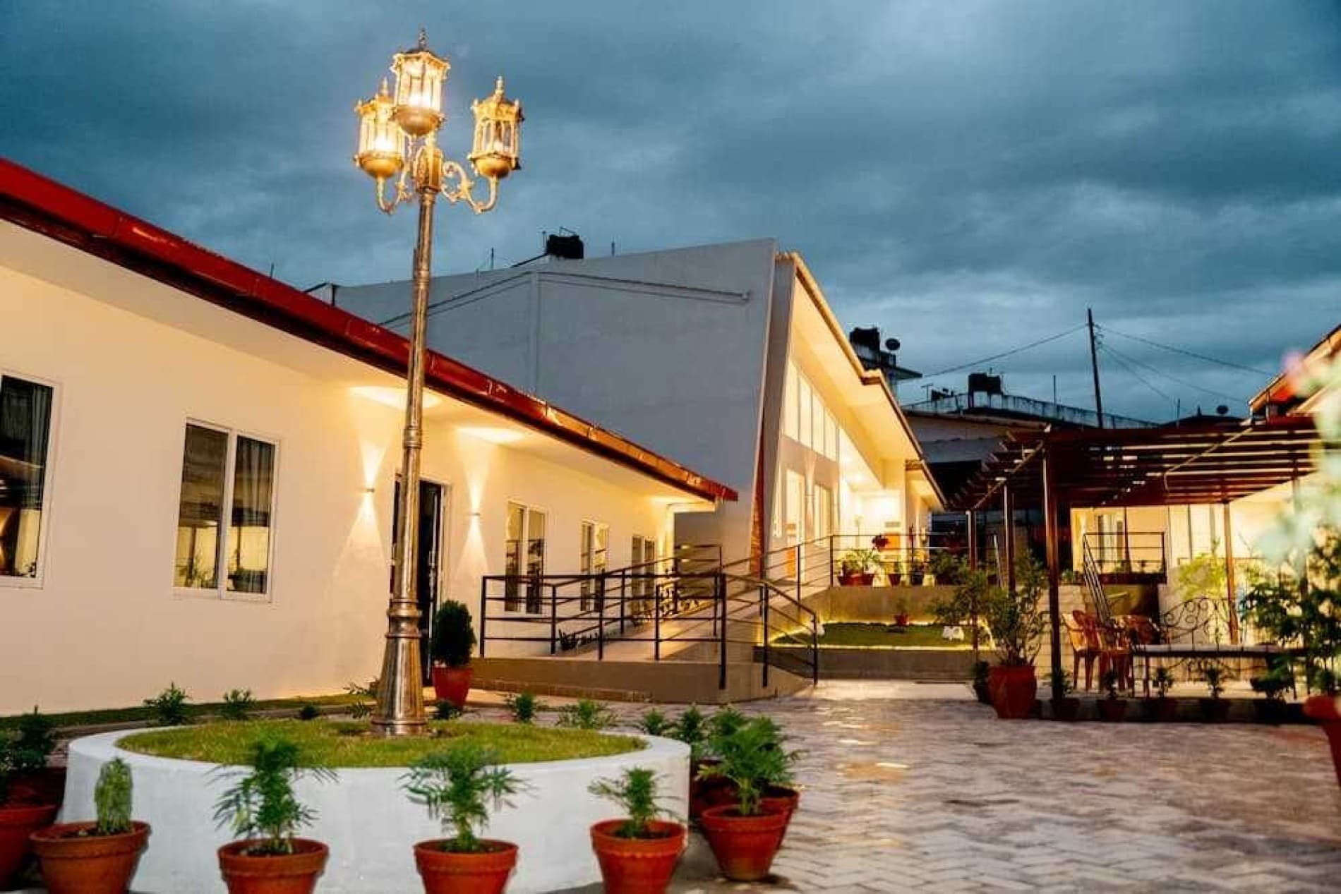 A Naman Care Home courtyard at dusk — ornate lamp post, red-roof veranda, potted plants